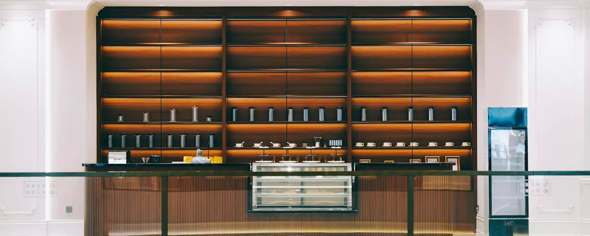 A modern shop counter with softly lit wooden shelves of small bottles